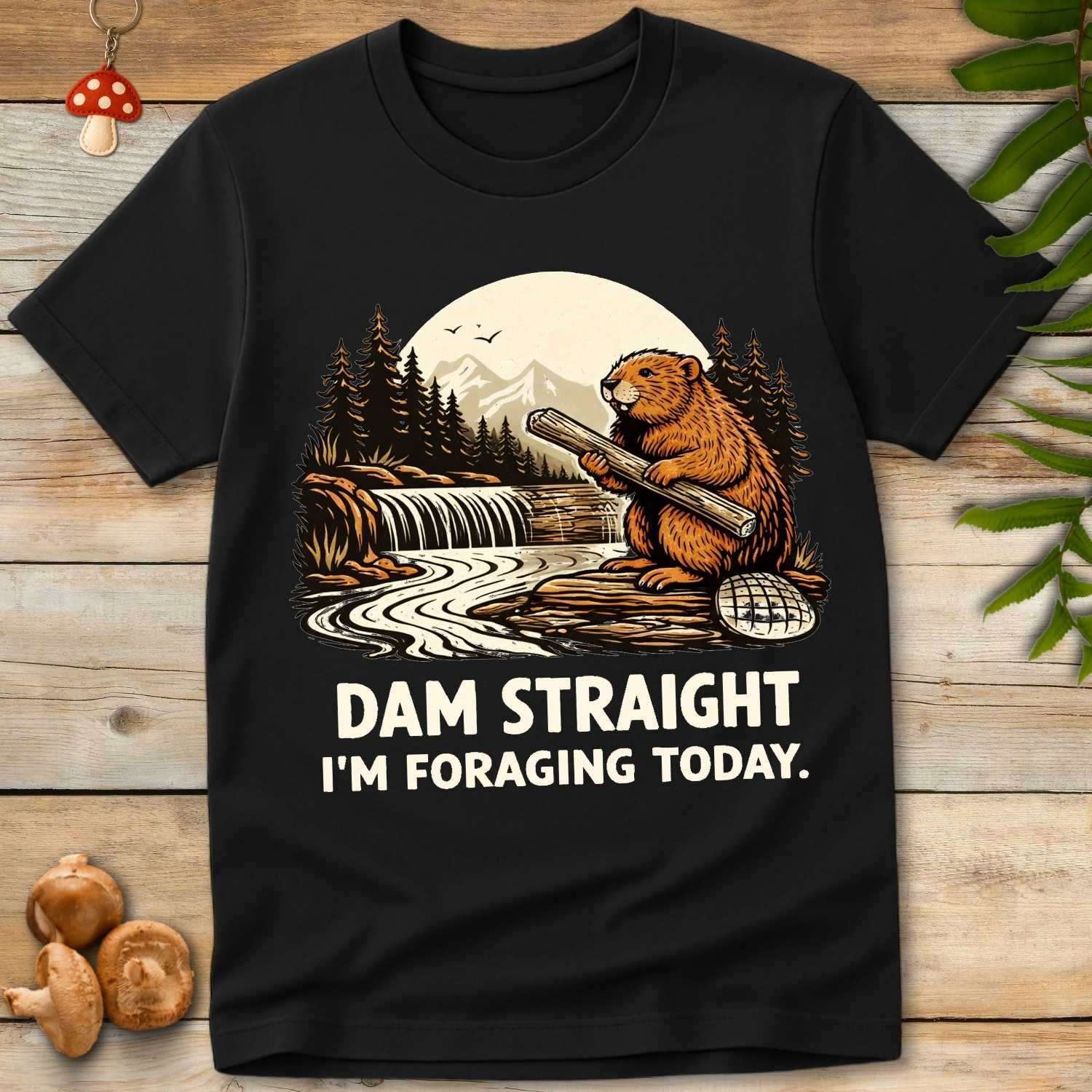 Vintage style illustration of a beaver holding a log by a river dam with mountains and pine trees, reading “Dam Straight I’m Foraging Today”.
