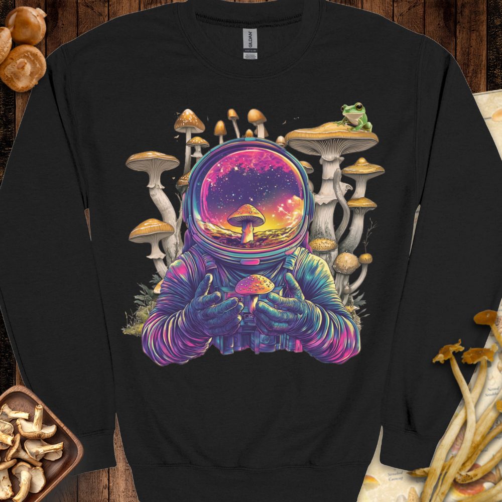 Psychedelic astronaut holding a glowing mushroom with a galaxy reflection in the helmet, surrounded by surreal mushrooms and a frog — featured on the Astromushroom Sweatshirt from Mushy Tees