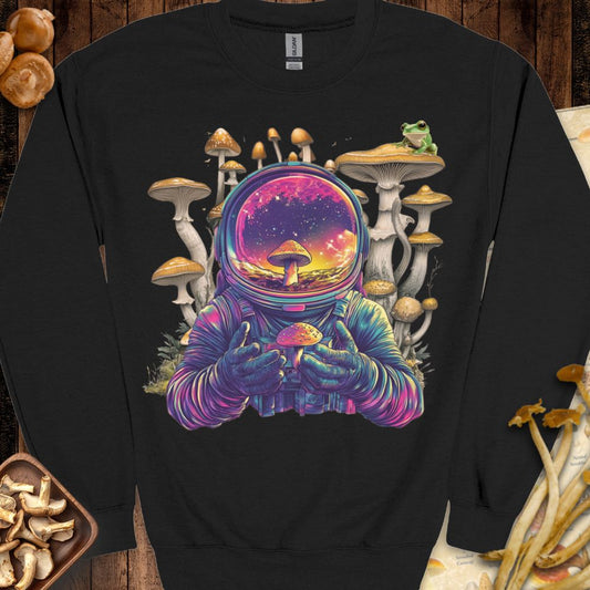 Psychedelic astronaut holding a glowing mushroom with a galaxy reflection in the helmet, surrounded by surreal mushrooms and a frog — featured on the Astromushroom Sweatshirt from Mushy Tees