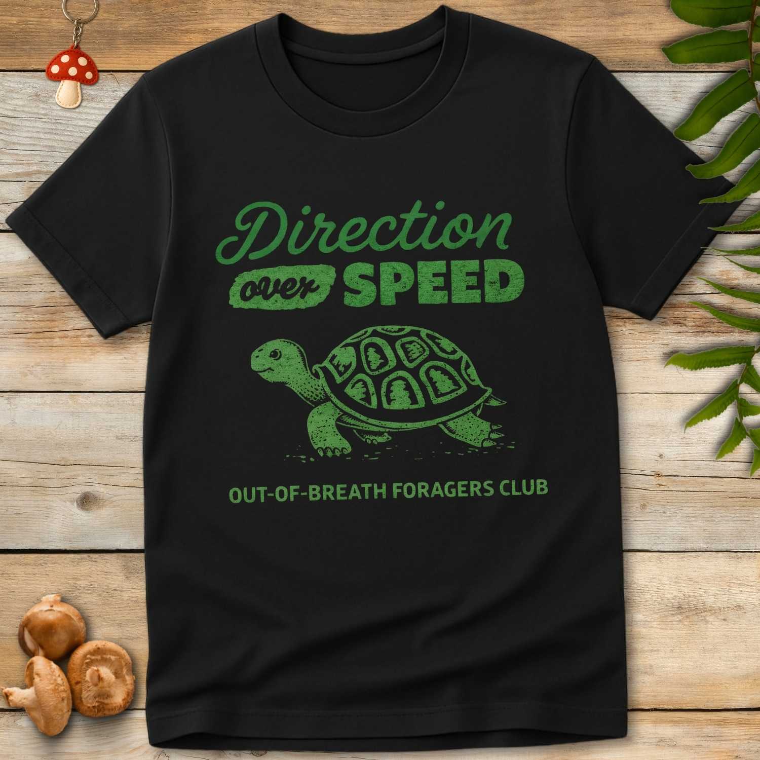 Green vintage-style t-shirt design featuring a tortoise with forest symbols on its shell and the phrase “Direction Over Speed – Out-of-Breath Foragers Club”