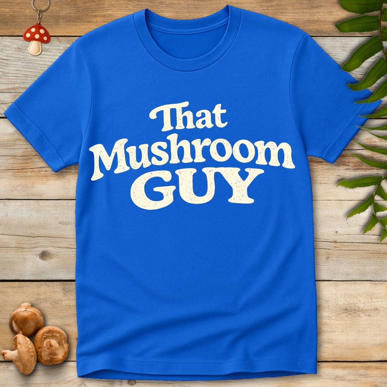 Retro style typography reading “That Mushroom Guy” in a bold cream font on a blue shirt 