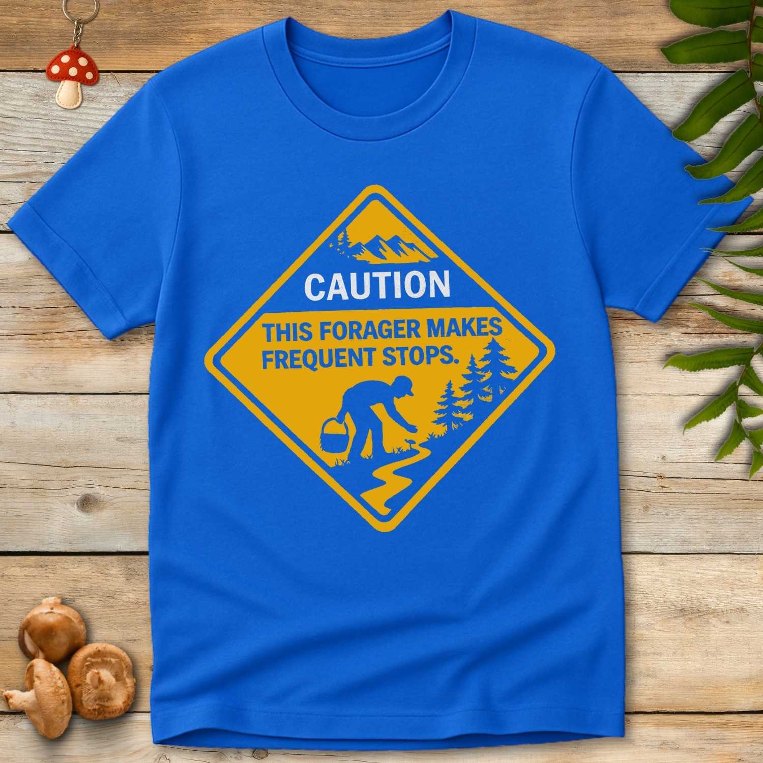 Yellow caution sign-style t-shirt graphic featuring a person foraging on a trail with the text “Caution: This Forager Makes Frequent Stops”