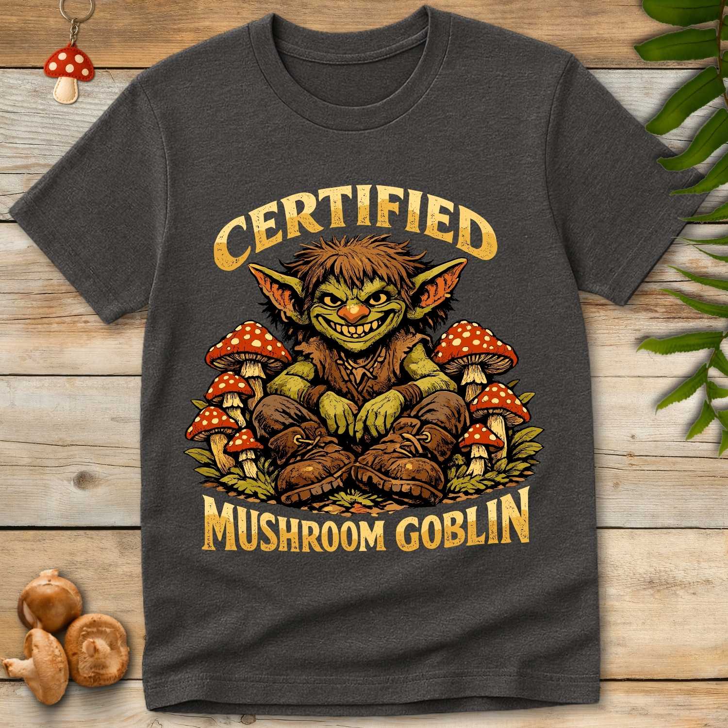 Smiling green goblin sitting among red and white toadstool mushrooms with the words "Certified Mushroom Goblin" in a fantasy-inspired vintage design.