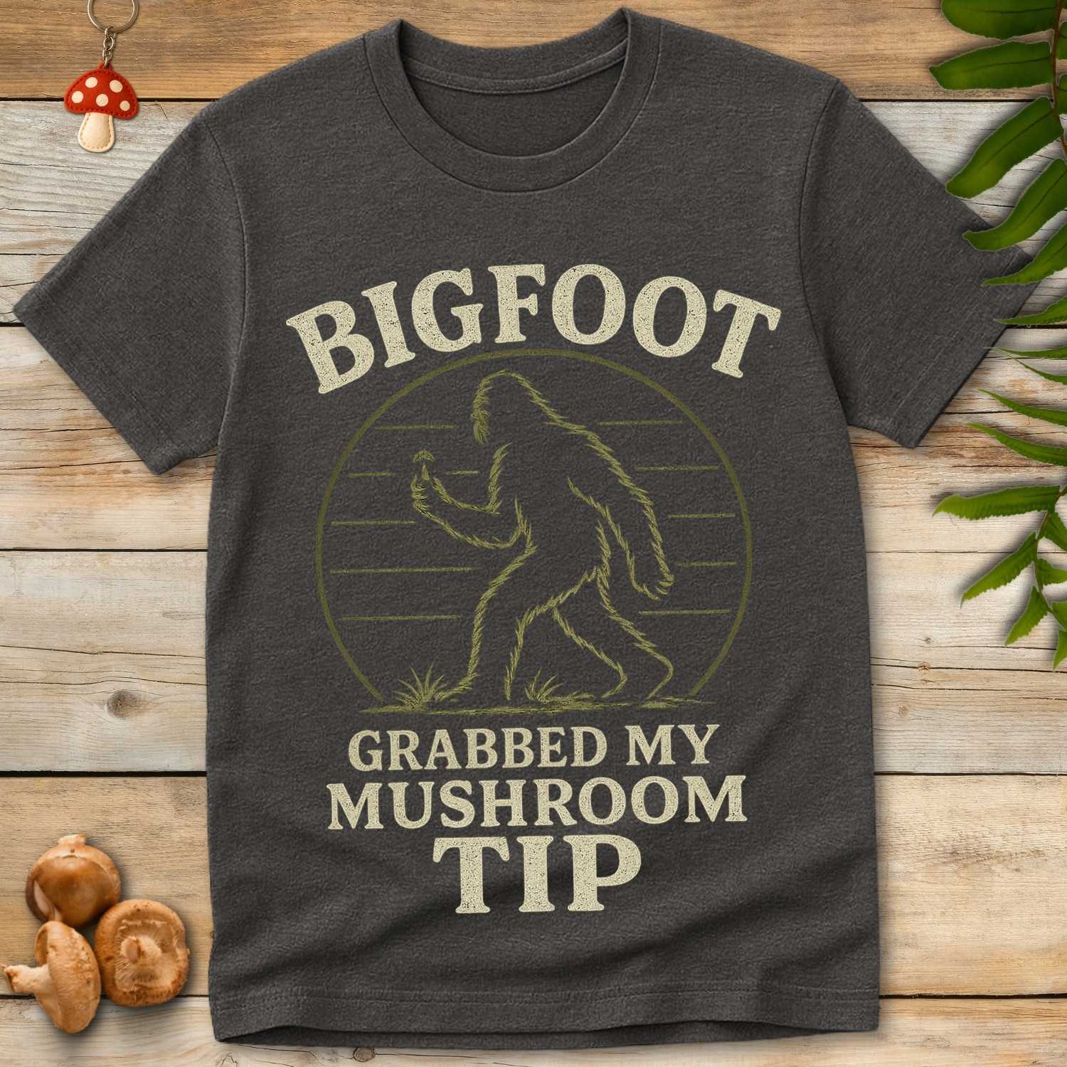 Mushroom Tip Tee featuring Bigfoot holding a mushroom with retro vintage forest artwork and funny mushroom hunting humor.