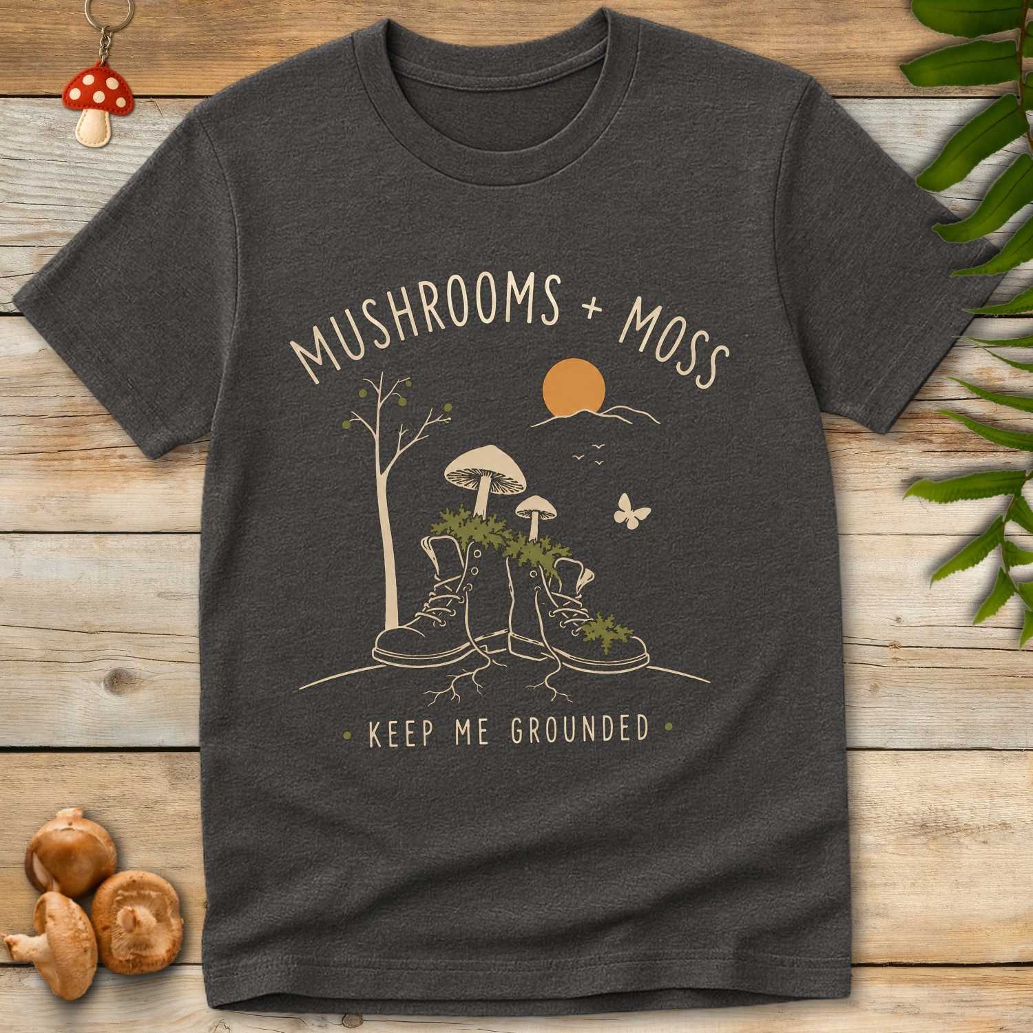 Shroom Moss Tee featuring moss-covered hiking boots with woodland mushrooms, roots, trees, and peaceful cottagecore forest artwork.