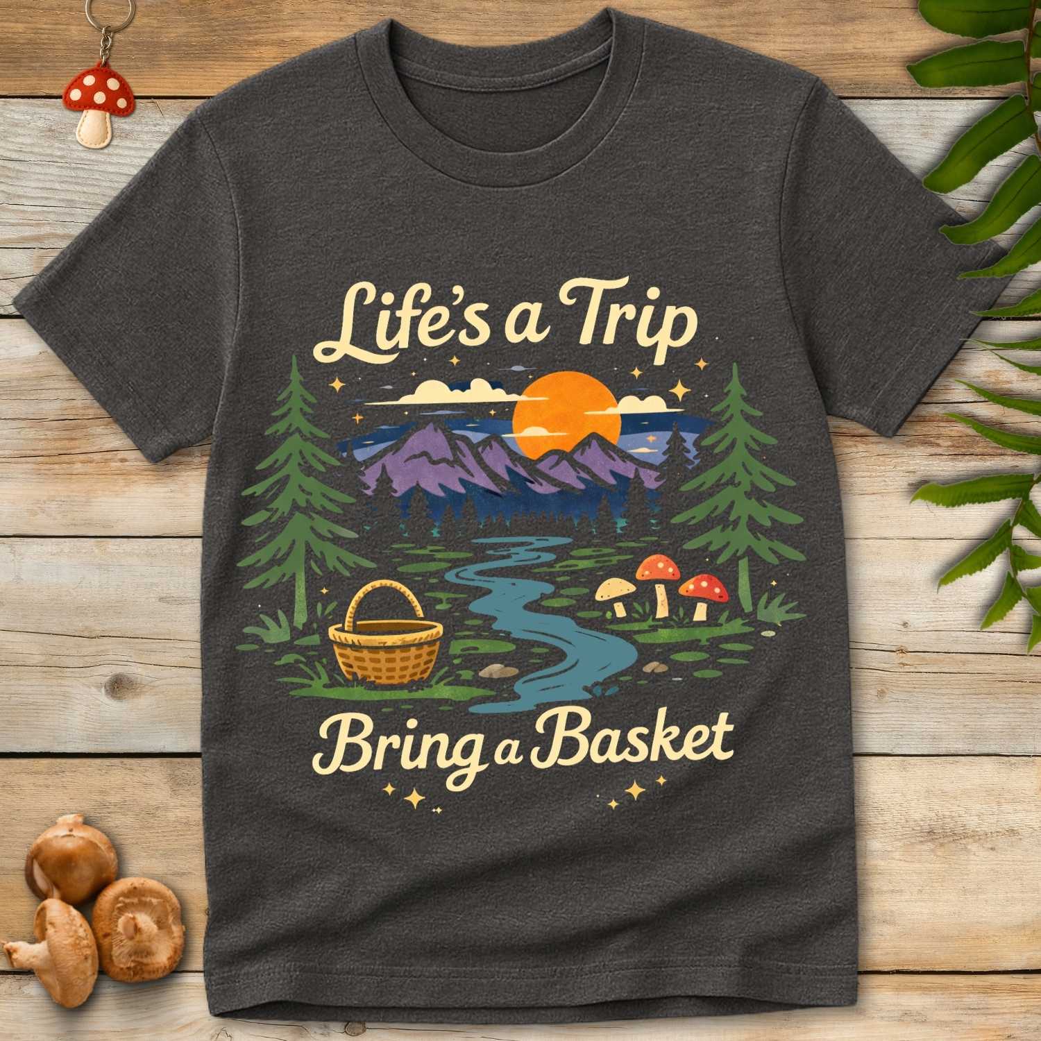 Retro forest landscape with mountains, sunset, mushrooms, and a foraging basket with the phrase “Life’s a Trip Bring a Basket”.