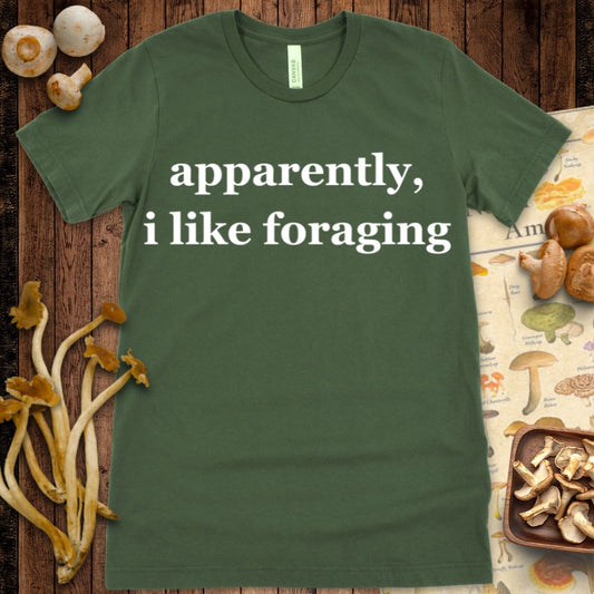 Minimalist T-shirt design with white text on black reading “apparently, i like foraging” in a bold serif font.