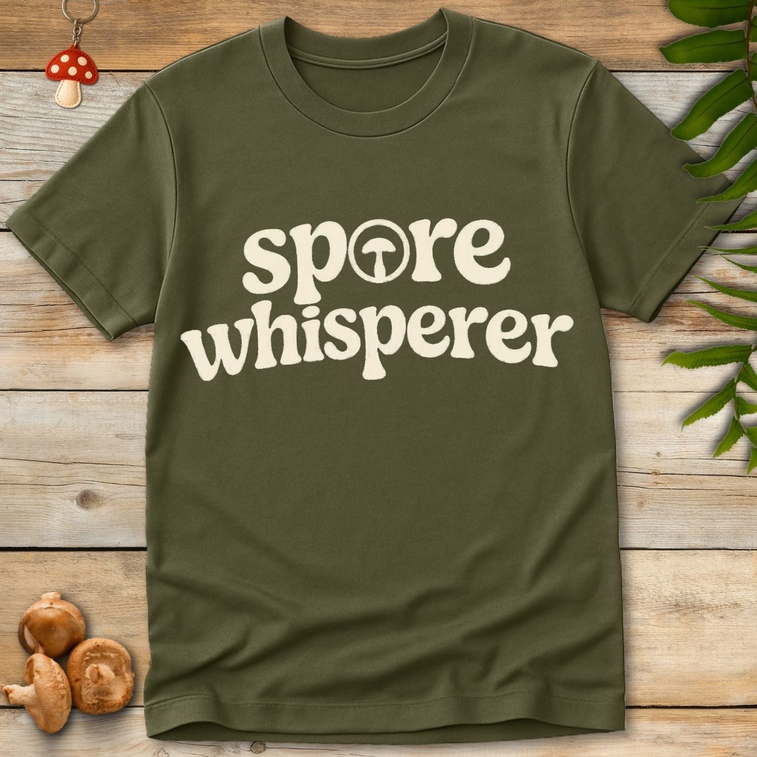 Retro style typography reading “spore whisperer” with a small mushroom icon integrated into the lettering on a green shirt.