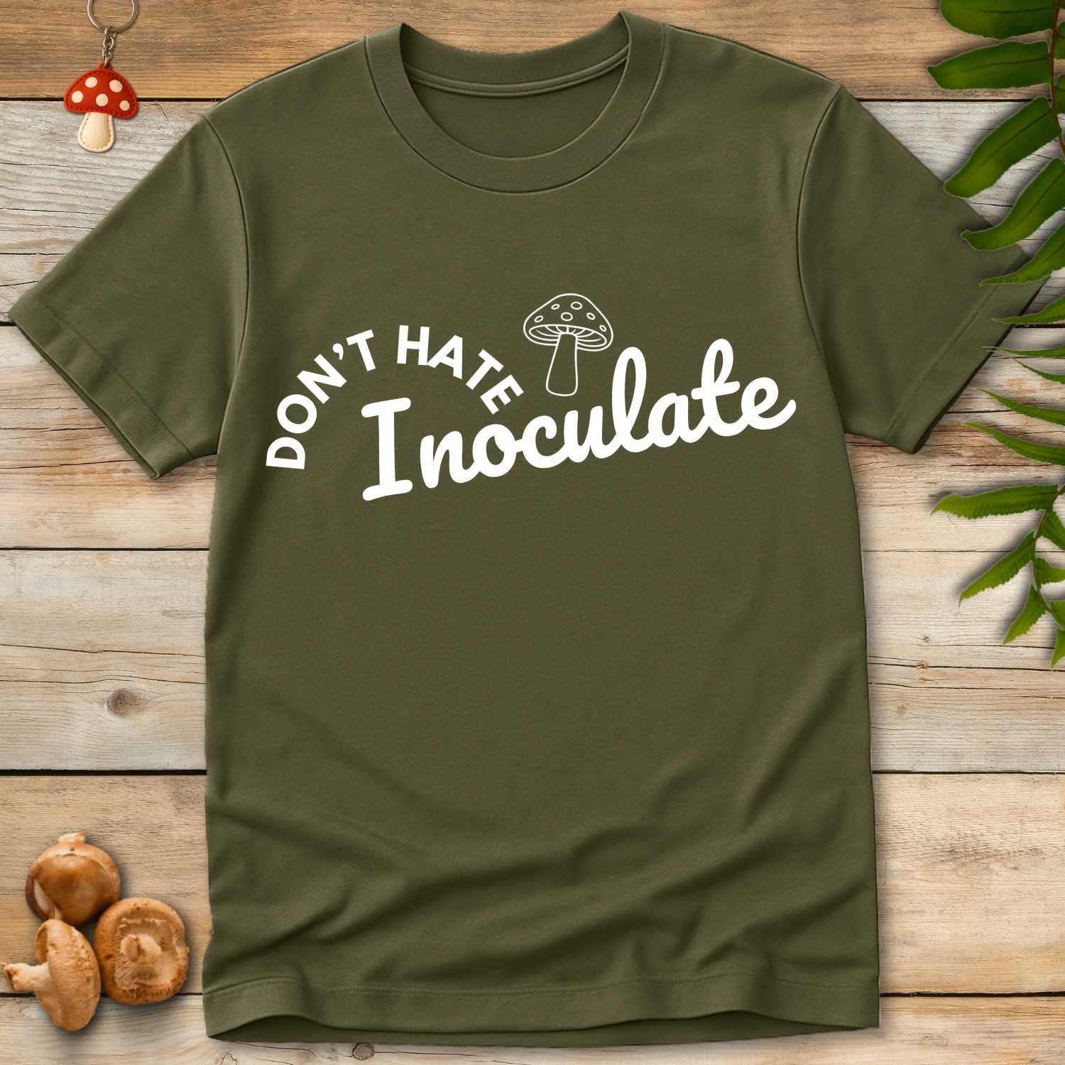 Green T-shirt with white text “Don’t Hate Inoculate” and a cartoon mushroom above the script