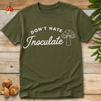 Green T-shirt with white text “Don’t Hate Inoculate” in curved bold and script fonts, with line-art mushroom illustration