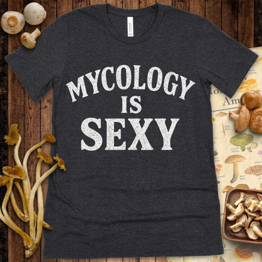 Black T-shirt design with large white text reading “Mycology is Sexy” in bold, arched lettering