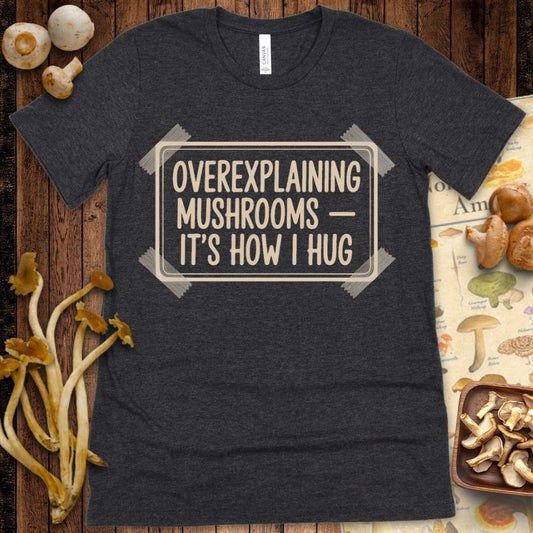 Cream text reading “Overexplaining Mushrooms — It’s How I Hug” inside a faux label frame with tape corners on a black background