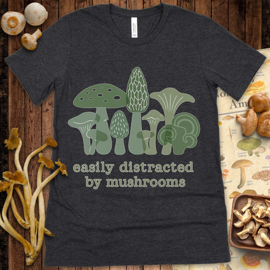 Illustrated green mushrooms with the text “easily distracted by mushrooms” in playful font on a T-shirt design.