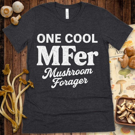 Black T-shirt design with bold white text that says "One Cool MFer – Mushroom Forager" in a mix of block and script fonts