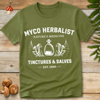 Green T-shirt with vintage white graphic reading “Myco Herbalist – Nature’s Medicine – Tinctures & Salves – Est. 1890” with mushroom and bottle illustrations