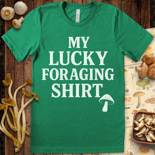 Black T-shirt design with bold white text saying "My Lucky Foraging Shirt" and a small illustrated mushroom