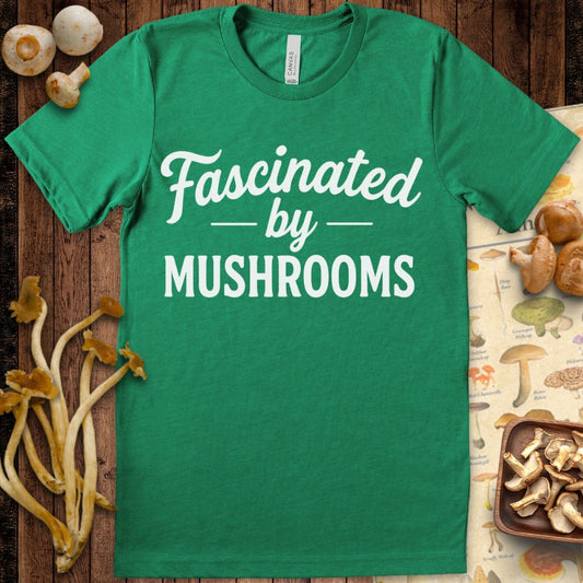 Green T-shirt design with white text saying “Fascinated by Mushrooms” in a mix of script and bold block fonts