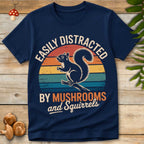 Navy blue t-shirt with a graphic of a squirrel and text 'Easily Distracted by Mushrooms and Squirrels' on a wooden surface.