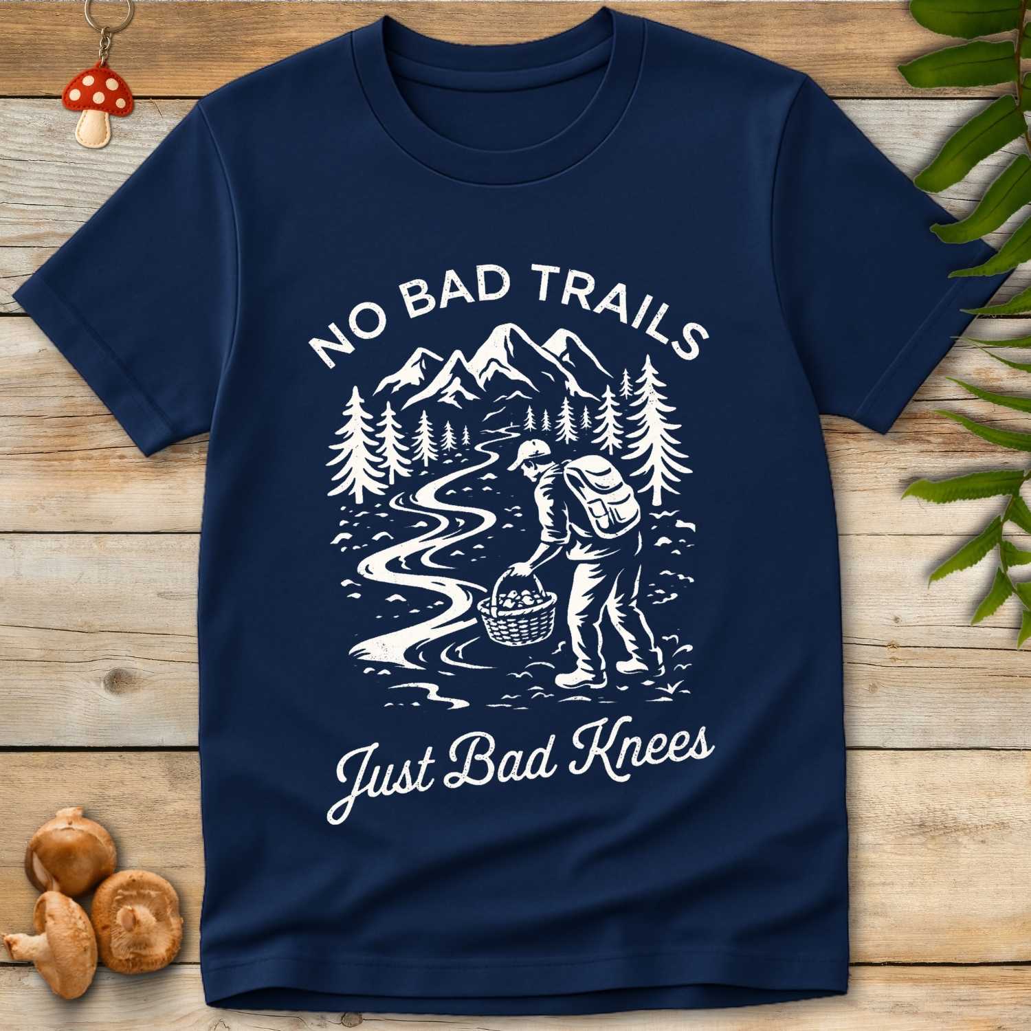 white t-shirt design of a hiker with a mushroom basket on a mountain trail with the phrase “No Bad Trails, Just Bad Knees”
