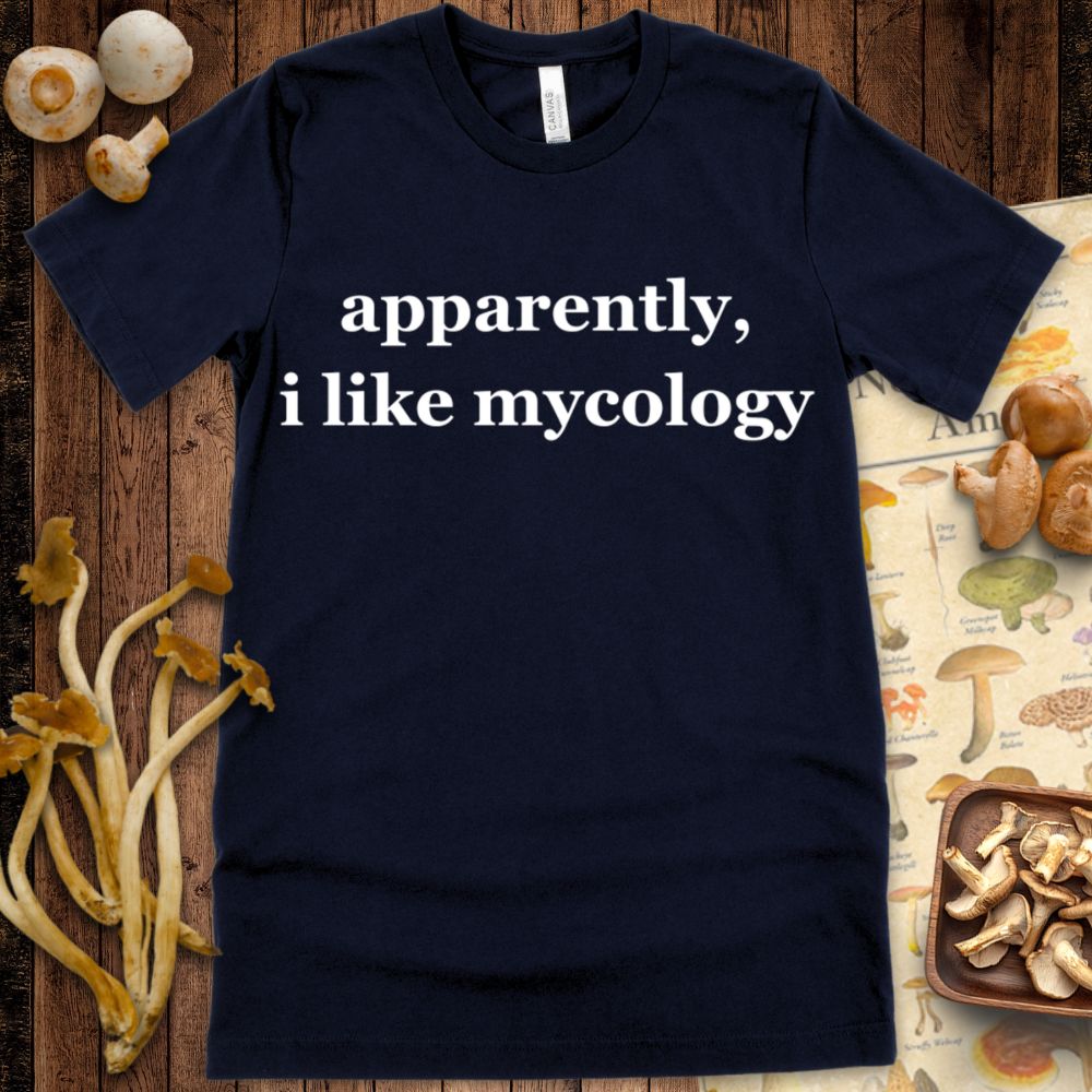 Minimal navy T-shirt design with bold white text saying “apparently, i like mycology” in a clean serif font.